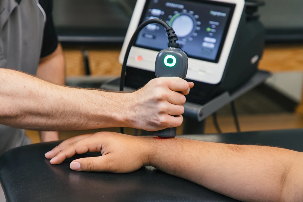 LightForce laser handpiece near a patient’s wrist with console controls visible