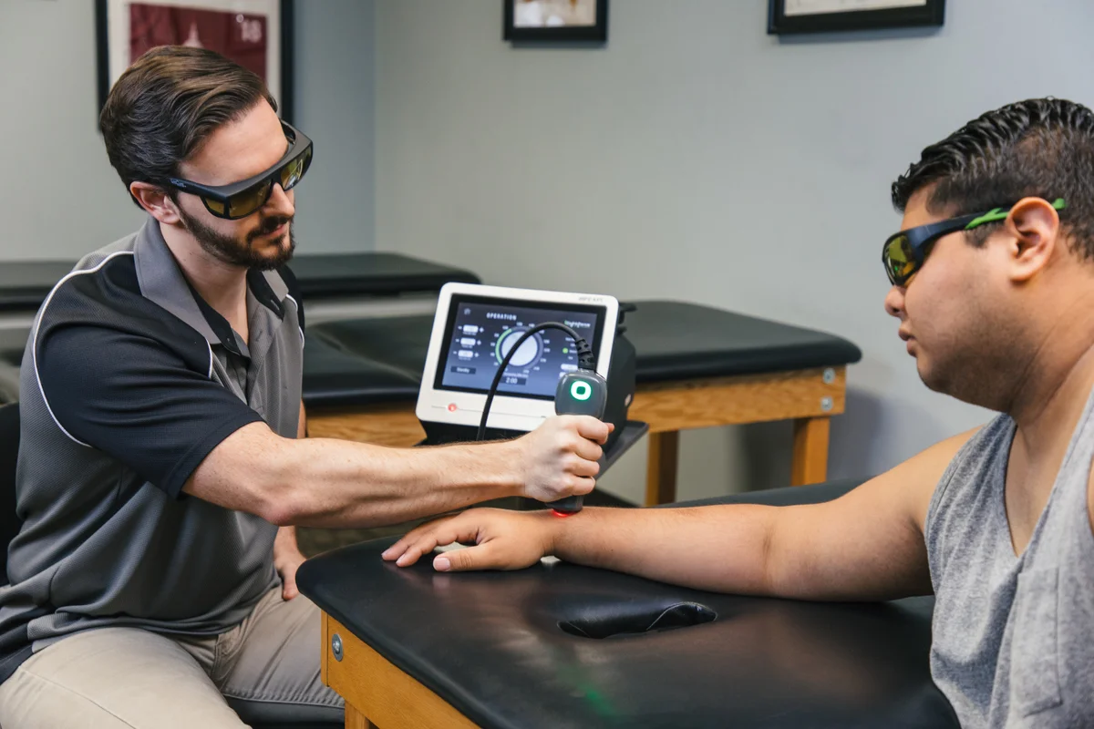 Clinician and patient beside a LightForce laser console during a wrist application